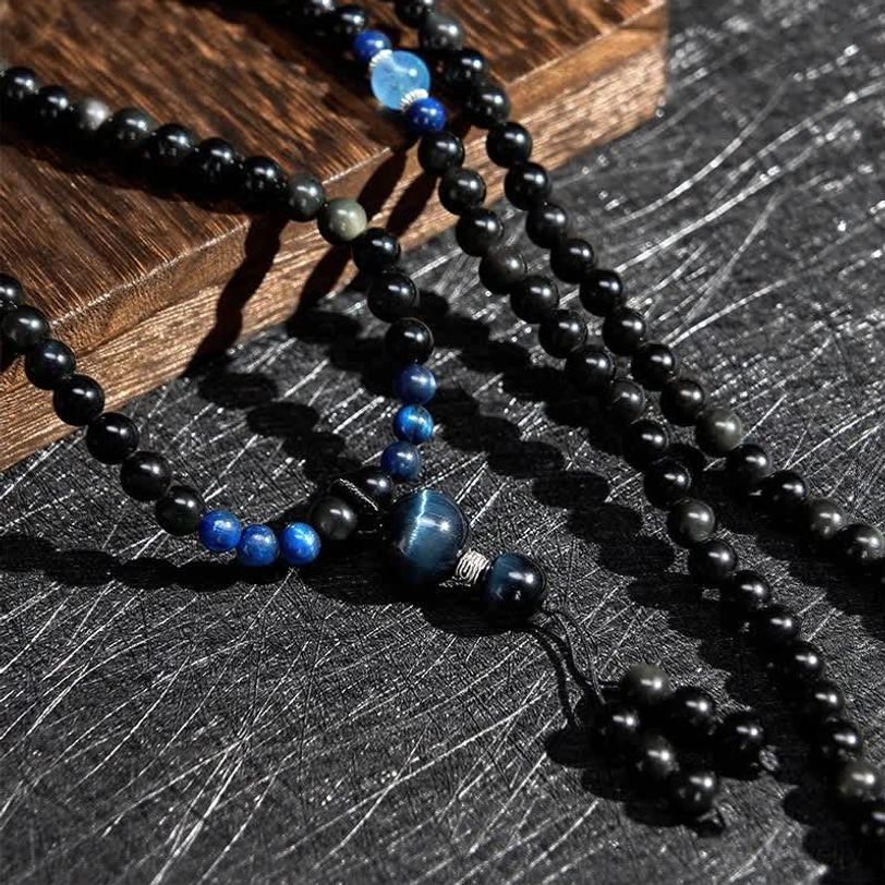 Close-up detailed view of Black Obsidian 108 bead mala links and central blue stone accent with tassel end on wooden block