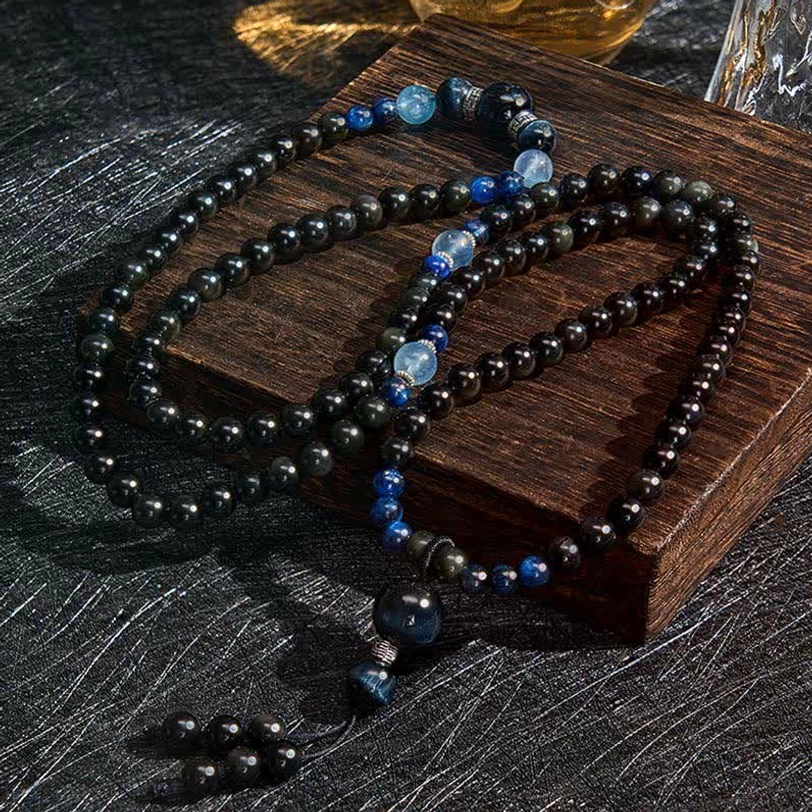 Loose Black Obsidian mala beads and strands arranged on wooden coaster, displaying individual bead quality and blue decorative stone details