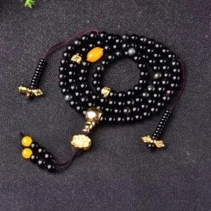 108 black obsidian mala bracelet with lotus tassel, flat lay display showing glossy round beads with gold hardware and yellow accent beads
