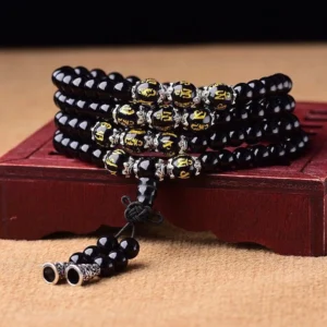 Black Obsidian 108-bead mala bracelet with gold-carved mantra beads and silver tassel on wooden display stand, top-down spiritual jewelry photography