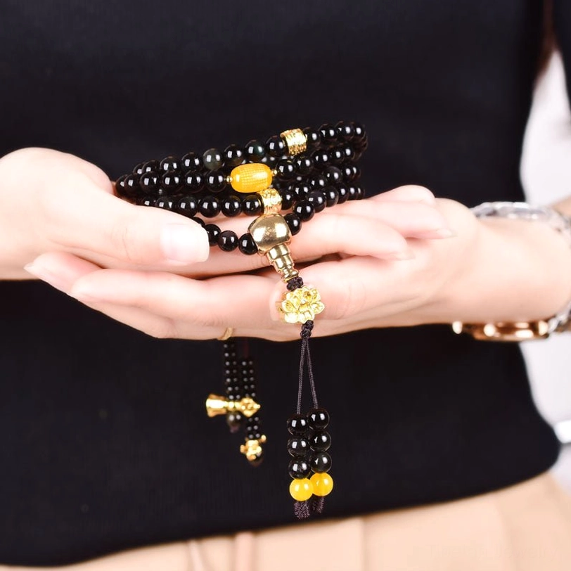 Person wearing 108 bead obsidian mala bracelet on wrist, showcasing black beads with gold accents and yellow spacer beads in real wear