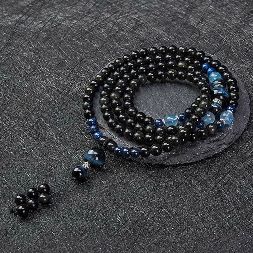 Complete Black Obsidian Tibetan mala necklace arranged in circle on round coaster, showing full strand with accent beads and tassel charm