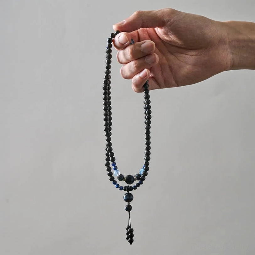Black Obsidian 108 bead mala necklace held by hand against white background, displaying single strand with blue accent beads and wearable length