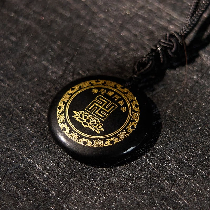 Round black obsidian pendant top-down view showing golden border and engravings