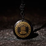 Black obsidian Buddhist pendant with golden swastika and lotus engravings on dark leather background