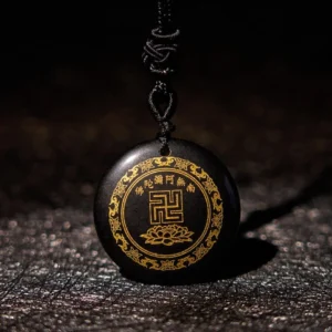 Black obsidian Buddhist pendant with golden swastika and lotus engravings on dark leather background