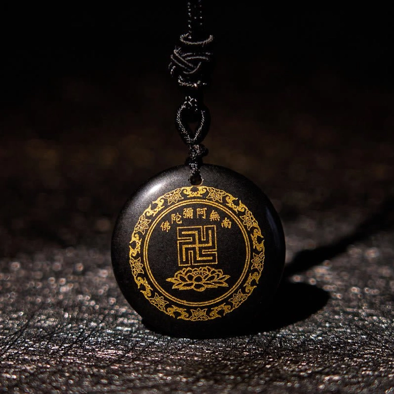 Black obsidian Buddhist pendant with golden swastika and lotus engravings on dark leather background