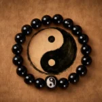 Black Obsidian Yin Yang protection bracelet flat lay on brown leather, showing engraved Yin Yang bead among polished black beads