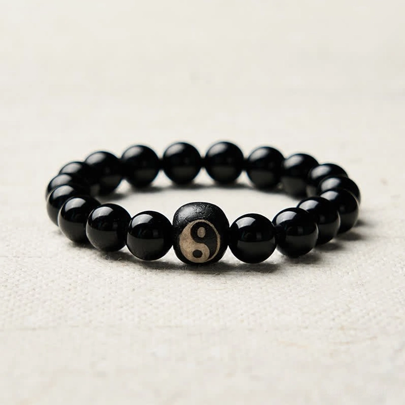 Black Obsidian Yin Yang protection bracelet close-up on white background, central engraved Yin Yang bead detail shot