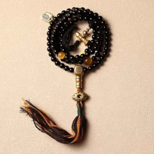 Black onyx 108 mala bracelet with cotton tassel and copper guru bead pendant on beige background, flat lay view