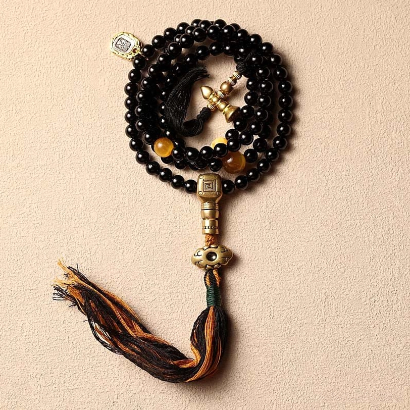 Black onyx 108 mala bracelet with cotton tassel and copper guru bead pendant on beige background, flat lay view