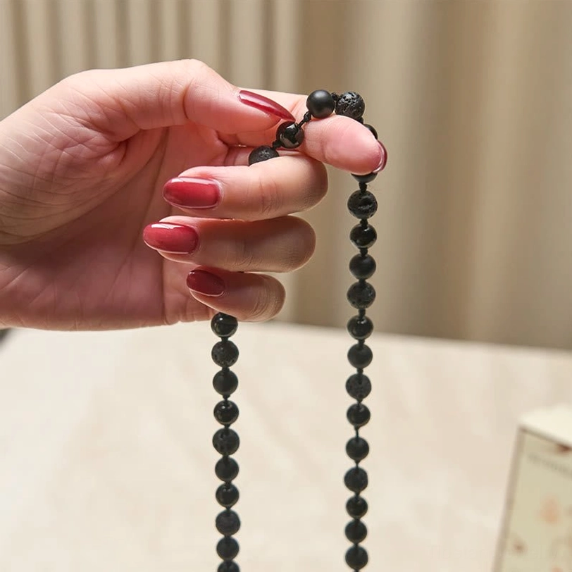 Close-up detail of 8mm black onyx and lava rock beads held in hand with manicure showing bead uniformity