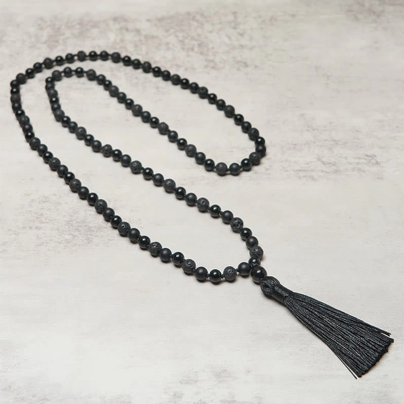 Side perspective flat lay of black beaded tibetan mala with silk tassel pendant on neutral surface