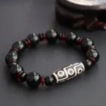 Black Onyx Nine-Eye Dzi Bead bracelet displayed on wooden stand, showing glossy black onyx beads with red spacer beads and hand-painted white nine-eye Dzi bead focal point