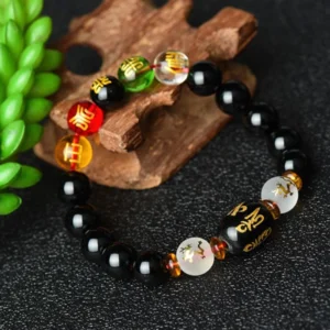 Handcrafted black onyx bracelet with polished beads and engraved barrel mantra beads arranged on wooden craft base with green succulent plant