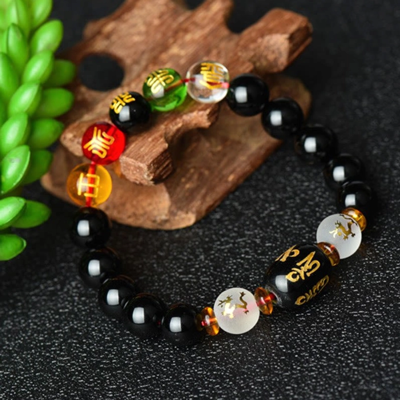 Handcrafted black onyx bracelet with polished beads and engraved barrel mantra beads arranged on wooden craft base with green succulent plant