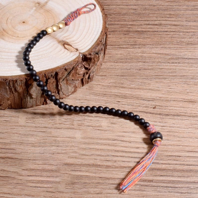 Extended layout of handmade Tibetan black onyx tassel bracelet showing braided tassel and metal spacer beads on wooden surface