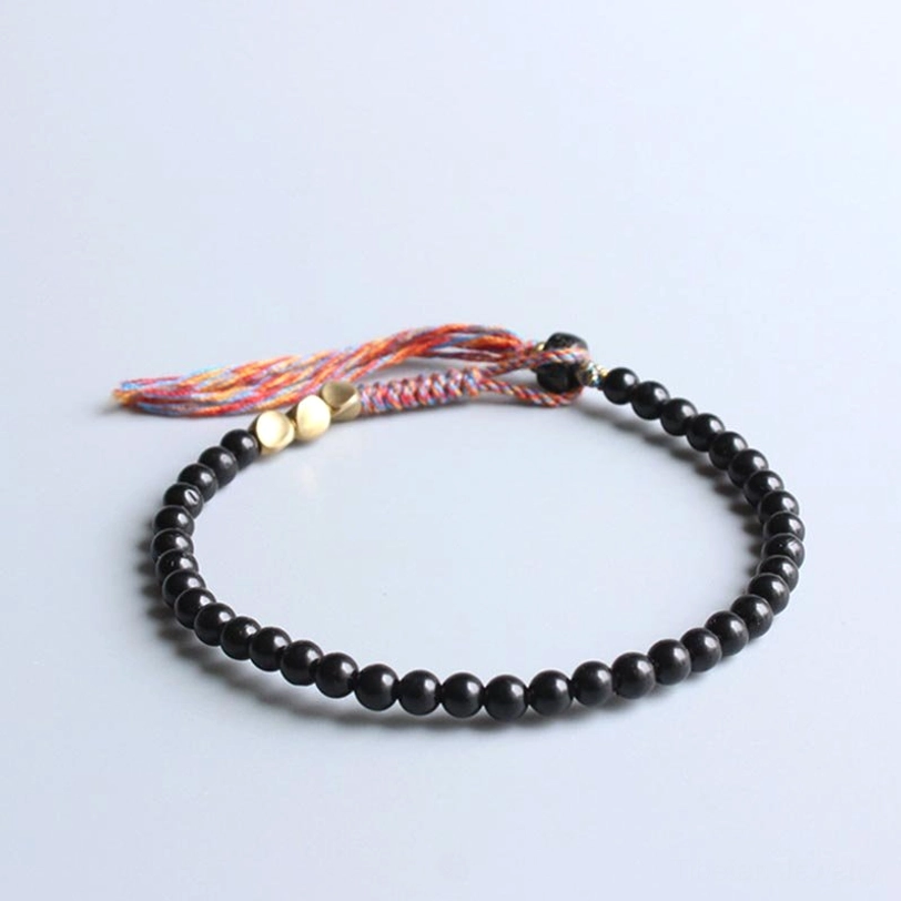 Tibetan black onyx protection bracelet featuring flat black beads with gold decorative accents and mixed-thread tassel detail