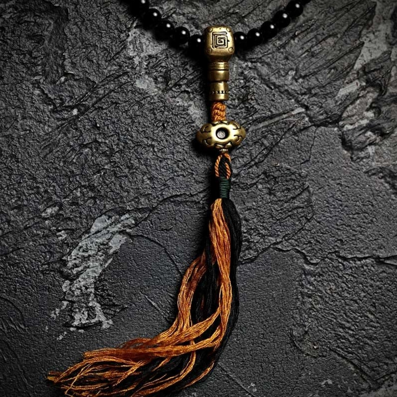 Close-up overhead view of black onyx and tiger eye mala beads with embossed brass spacer beads on dark stone texture background