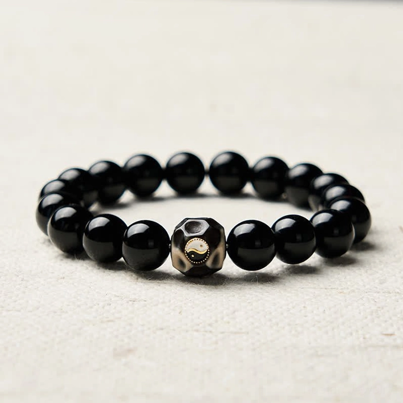 Black Onyx Yin Yang bracelet with uniform polished beads and faceted center charm on fabric background