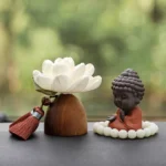 Black peach wood Buddha lotus meditation decoration with terracotta robe, white fabric flower, and prayer beads on natural wood base