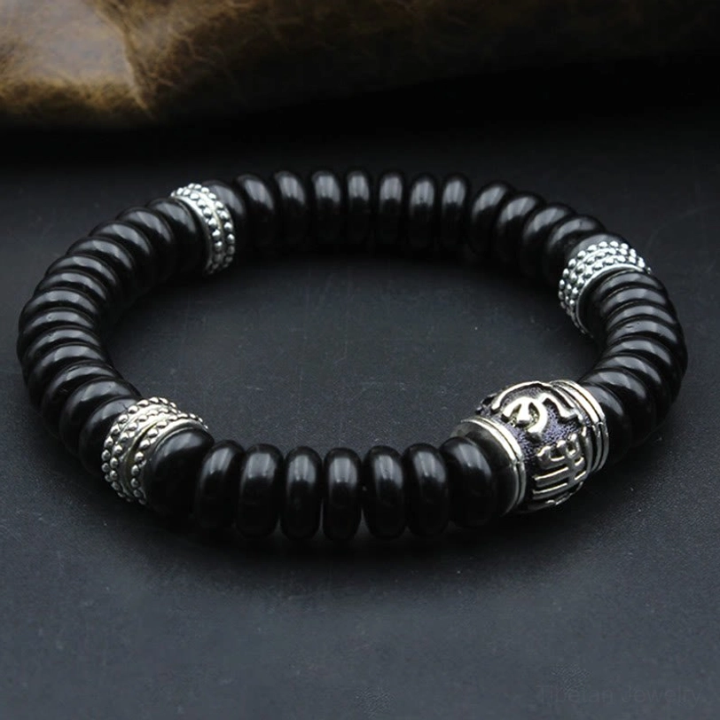 Detailed side view of black coconut shell bracelet showing engraved mantra bead, silver components, and elastic cord construction
