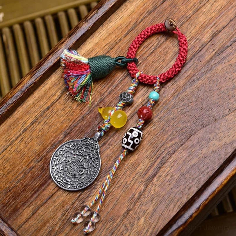 Black and white Dzi bead Tibetan amulet keychain featuring striped pattern, red rope, silver Bagua charm on wooden desk