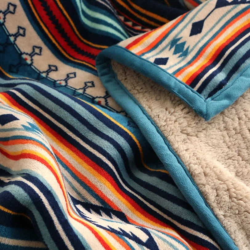 Flat lay close-up of blanket texture displaying clear tribal geometric print, soft plush fabric, and blue edge binding in studio lighting