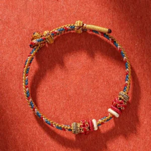Close-up of woven Tibetan protection bracelet featuring red, gold, and blue braided string with bead accents