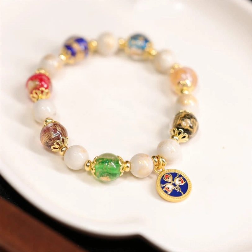 Blue God of Wealth Tibetan bracelet with blue enamel facial pendant, mixed colored glass beads, and metal hardware on ceramic display tray