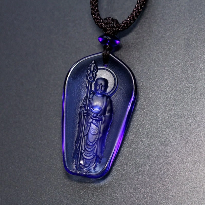 Deep blue Ksitigarbha Buddha Liuli crystal pendant with elongated oval shape, standing Bodhisattva with halo and staff, black braided cord with purple bead accent