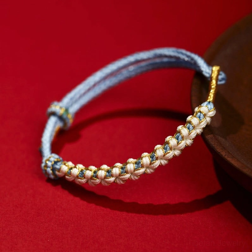 Light blue Tibetan braided bracelet with gold thread accents peach blossom knot design