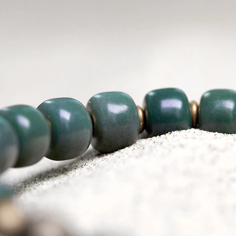 Macro close-up of Tibetan bodhi seed beads with bronze metal spacers on sandy surface, showing texture and craftsmanship