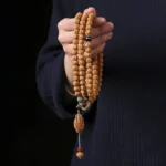 Bodhi seed mala bracelet with three-eye Dzi bead and Buddha hand tassel worn on wrist, first-person close-up view