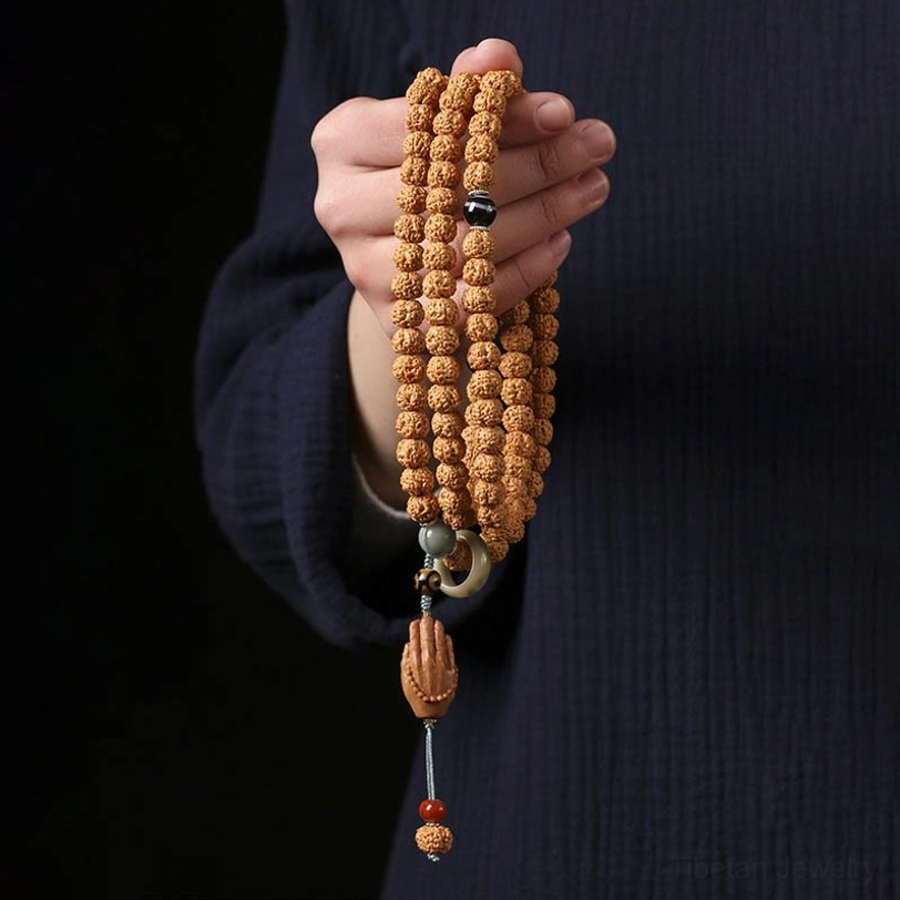 Bodhi seed mala bracelet with three-eye Dzi bead and Buddha hand tassel worn on wrist, first-person close-up view