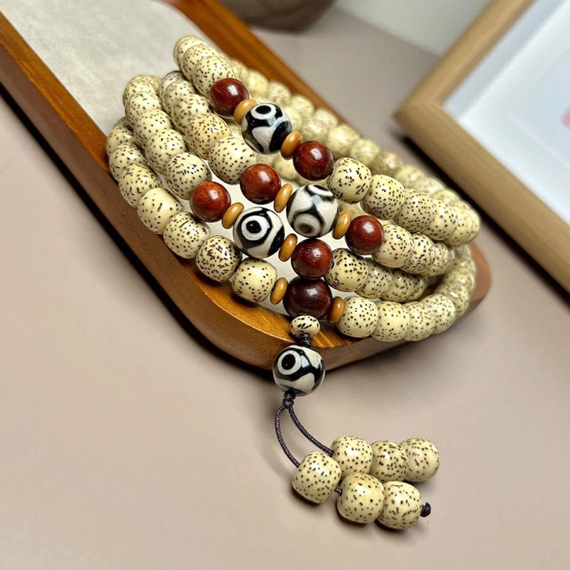 Close-up detail of 108 mala beads showing Bodhi seed texture, hand-painted Dzi bead, and intricate tassel pendant craftsmanship