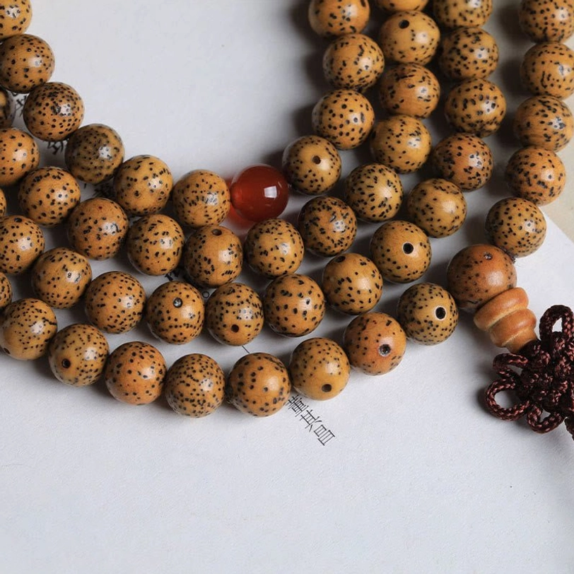 Tibetan bodhi seed mala bracelet with tassel showing spotted tan bodhi beads, red agate spacers, and dark red braided charm