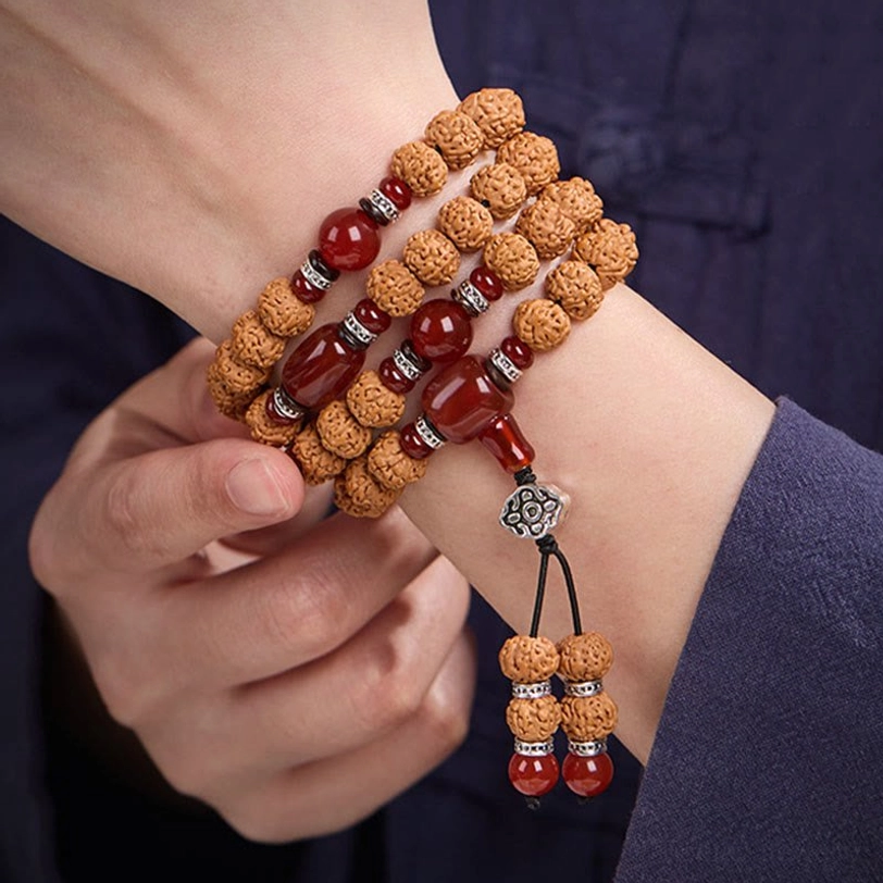 Top-down view of bodhi seed mala as wrist bracelet with multiple wraps, displaying tassel pendant with red agate and silver hardware details