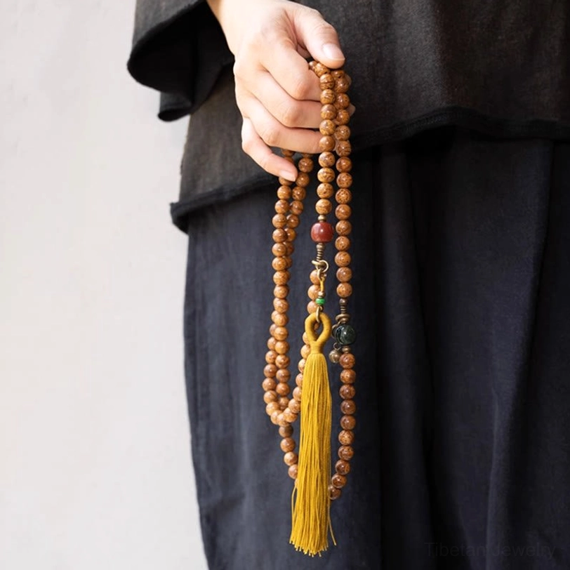 108 bodhi seed mala worn on wrist with tassel pendant and metal charms close-up