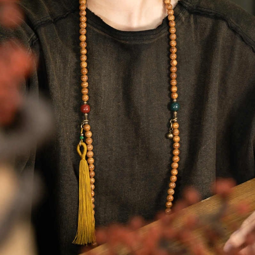 Bodhi seed mala bracelet worn on chest with mustard tassel and gemstone accents