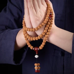 Front view of bodhi seed mala wrapped between two hands showing detailed tassel pendant, brown seeds with red agate and silver components