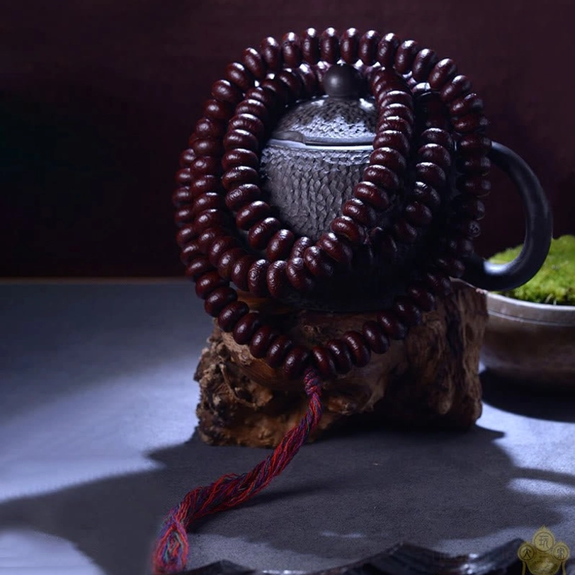 Complete wrapped 108 Purple Bodhi Seed mala coil with colorful tassel cord on wooden display stand