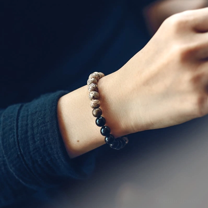 Close-up side view of worn Tibetan Bodhi bracelet with Black Obsidian and metal charms paired with dark green clothing
