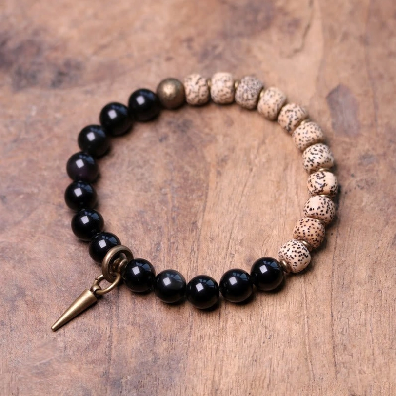 Tibetan Bodhi Seed and Black Obsidian protection bracelet featuring natural beads with brass spike pendant, displayed on wooden table from overhead view
