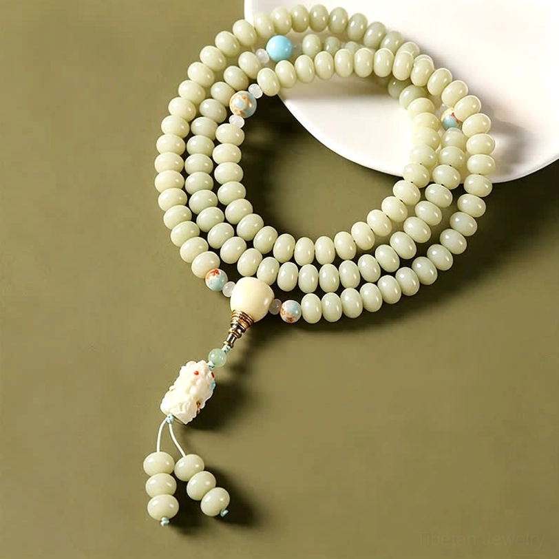 Hand-woven white bodhi seed mala with light green beads and blue accent beads on white plate background