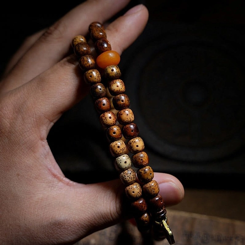 Zakiram bodhi seed bracelet held between fingers showing aged brown seeds, orange agate bead, and metal end clasp detail