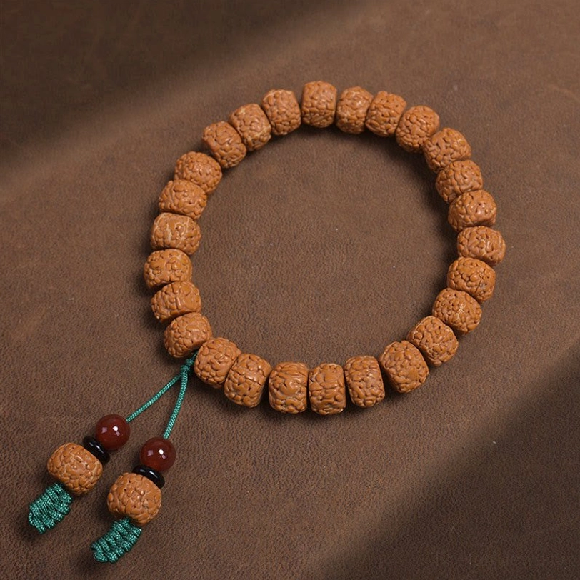 Top-down flat lay of bodhi seed prayer bracelet with cylindrical beads and tassel pendants on leather