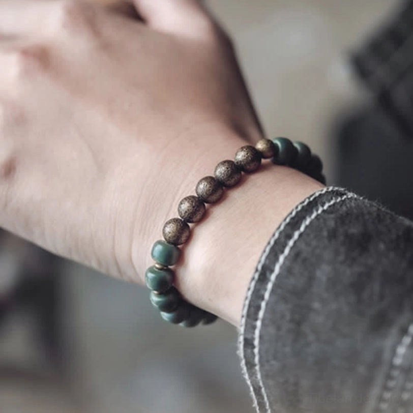 Close-up of bodhi seed copper bracelet worn on wrist indoors, displaying bronze and green beads with denim sleeve