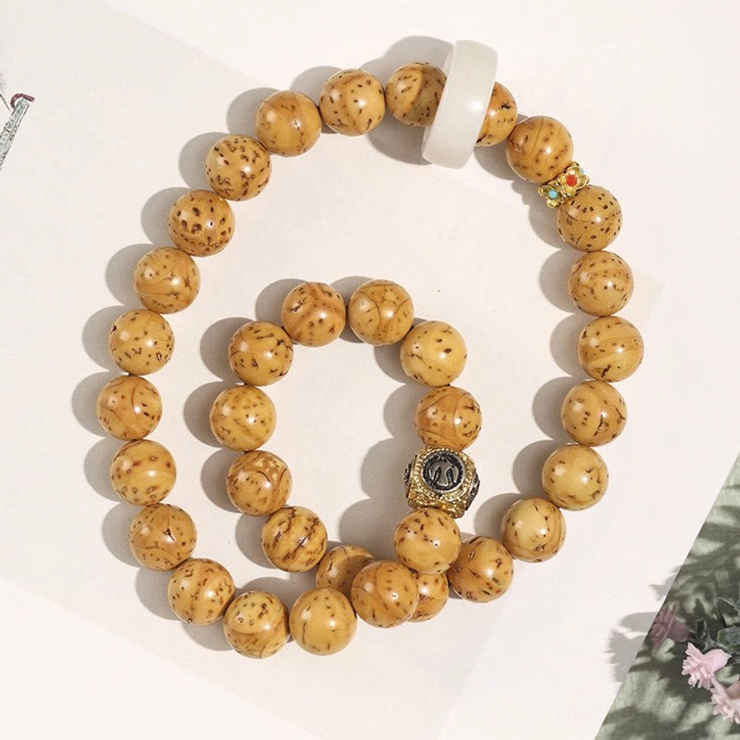 Light yellow spotted Bodhi seed beads double wrap bracelet with silver metal charm and white spacer ring on floral background