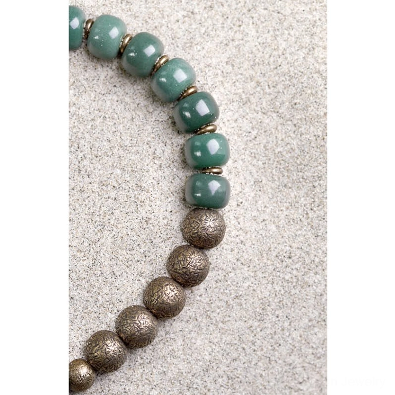 Close-up macro view of Tibetan bodhi seed copper bracelet beads on sandy surface, showing alternating green and bronze bead pattern